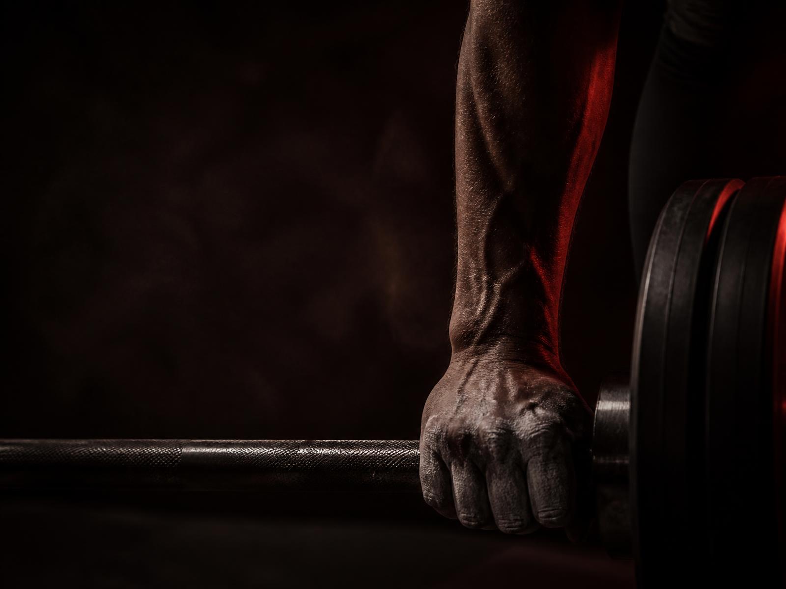 Athlete gripping a loaded barbell in dark red light